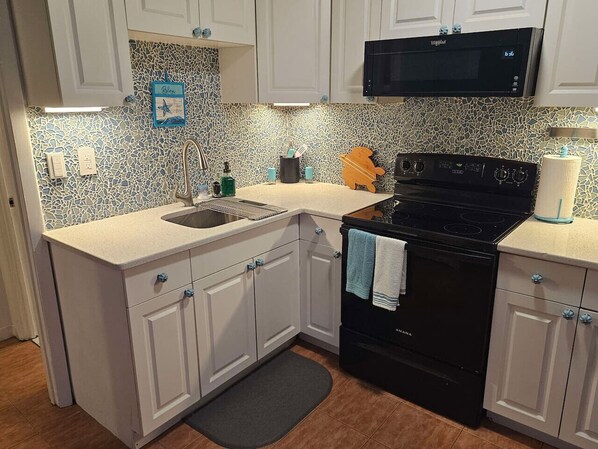 A kitchen with white cabinets, a black stove, a microwave, and a tiled backsplash.
