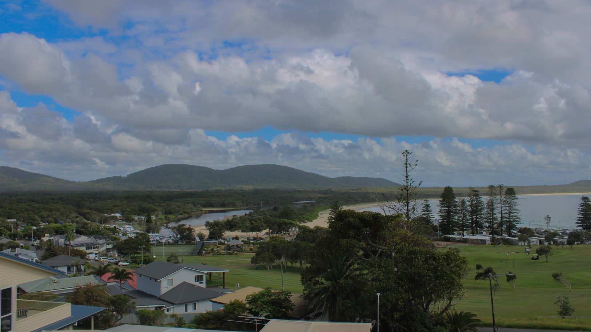 A coastal town with houses, a beach, and mountains in the background.