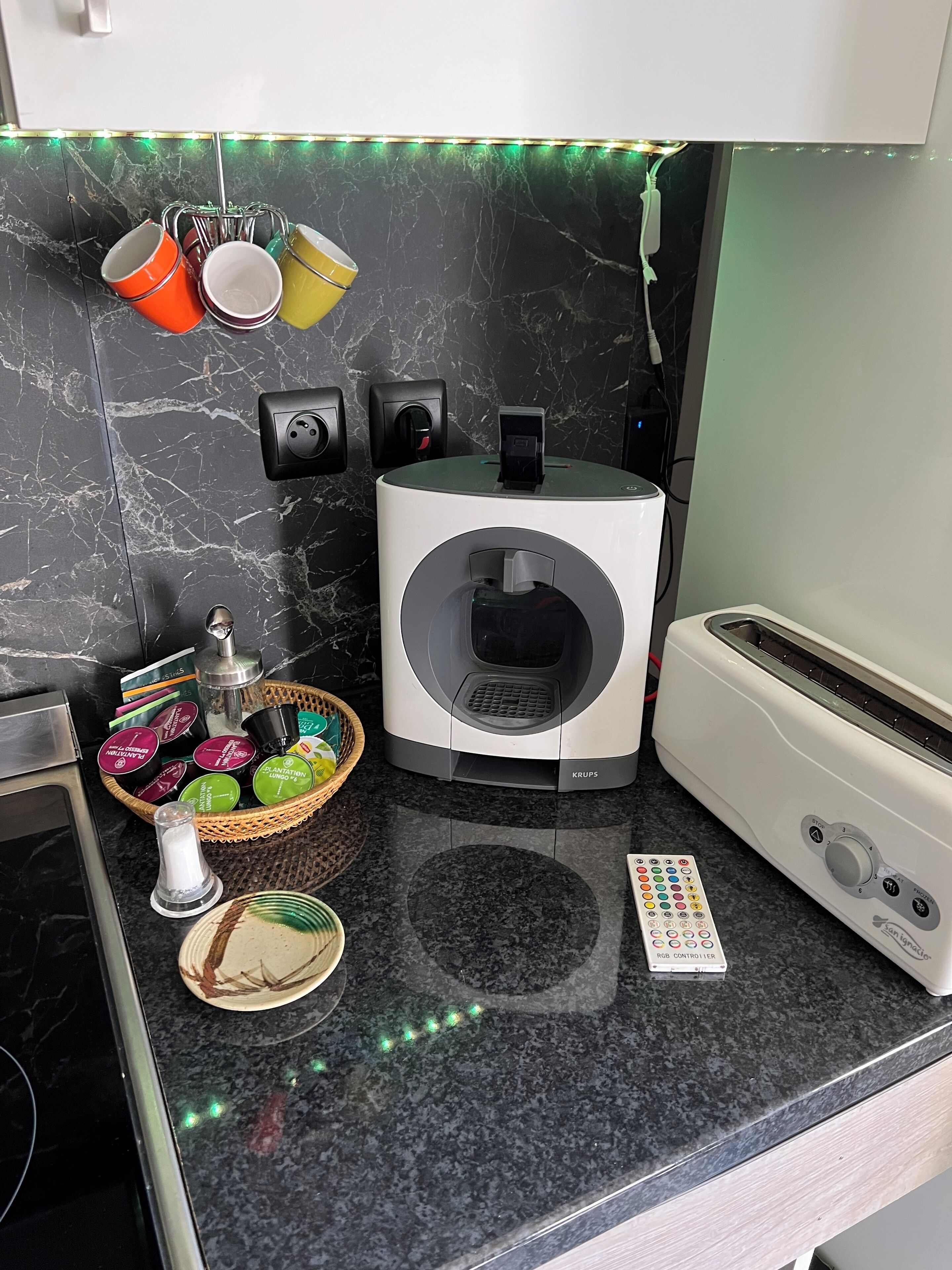 A kitchen with a modern design, featuring a built-in washing machine, a toaster, and a basket of toiletries.