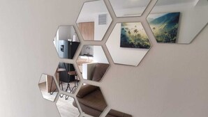 Una pared con espejos hexagonales dispuestos en un patrón de panal, reflejando una cocina con mesa y sillas.