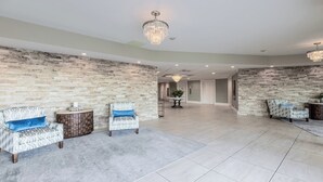 Una habitación amplia con una pared de piedra, dos sillones estampados, una mesita y un candelabro.