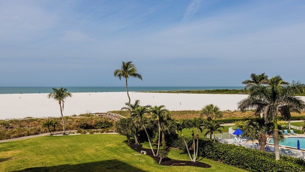 Vista a la playa con zona de piscina, palmeras y cielo despejado.