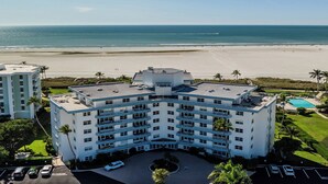 Un hotel de varios pisos con piscina en la azotea, situado cerca de una playa con vistas claras al océano.