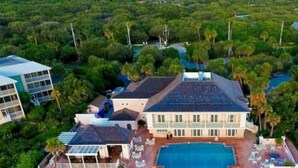 Vista aérea de una casa grande con piscina, rodeada de exuberante vegetación y una playa.