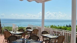 Un área de comedor al aire libre con mesas y sillas, con vista al océano.