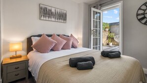 A bedroom with a bed, pillows, a nightstand, a lamp, a clock, and a view of the outside. - Chic 1Bed w/Patio Battersea (Greater London)