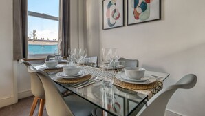 A dining table set for six with clear glassware and white plates, positioned near a window with a view of the sea. - Chic 1Bed w/Patio Battersea (Greater London)