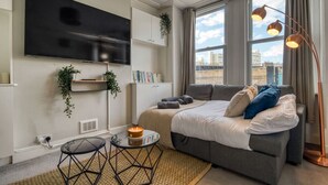 A modern bedroom with a large bed, a TV mounted on the wall, and a window with curtains. - Chic 1Bed w/Patio Battersea (Greater London)
