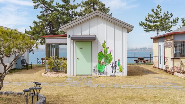 Un petit bâtiment d’un seul étage, avec une porte verte, une fresque représentant un cactus et un banc au premier plan.