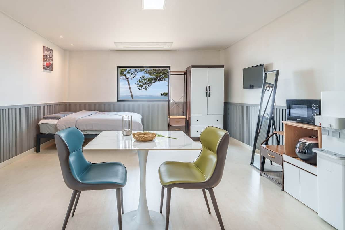 A compact hotel room with a bed, a small table with chairs, a television, and a kitchenette.