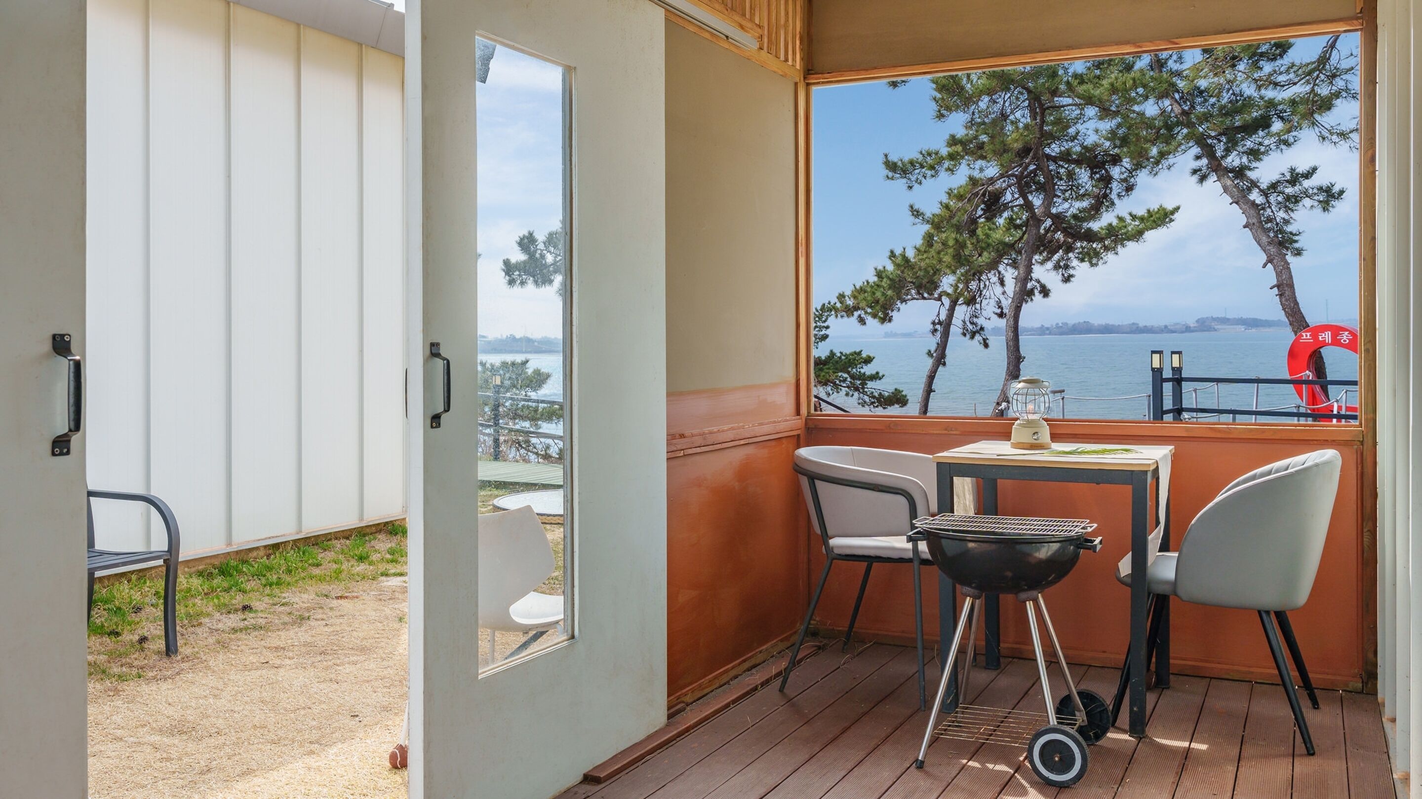 A balcony with a view of the sea, a table with chairs, and a grill.