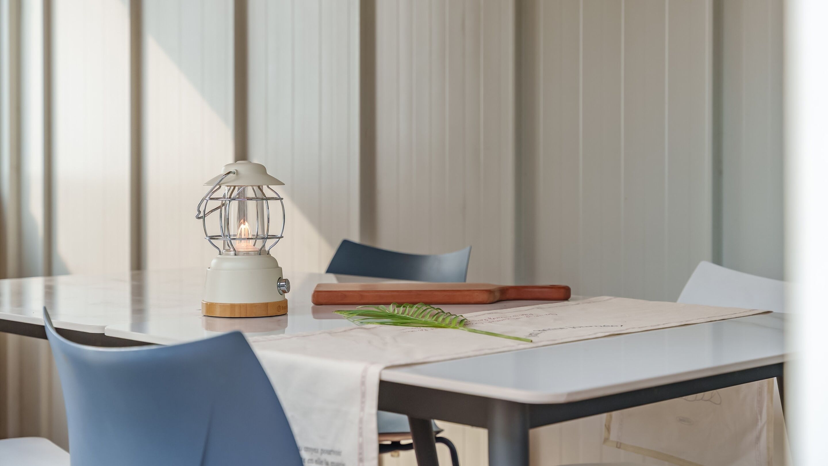 Una mesa con mantel blanco, un libro de madera, una hoja verde y un farol blanco.