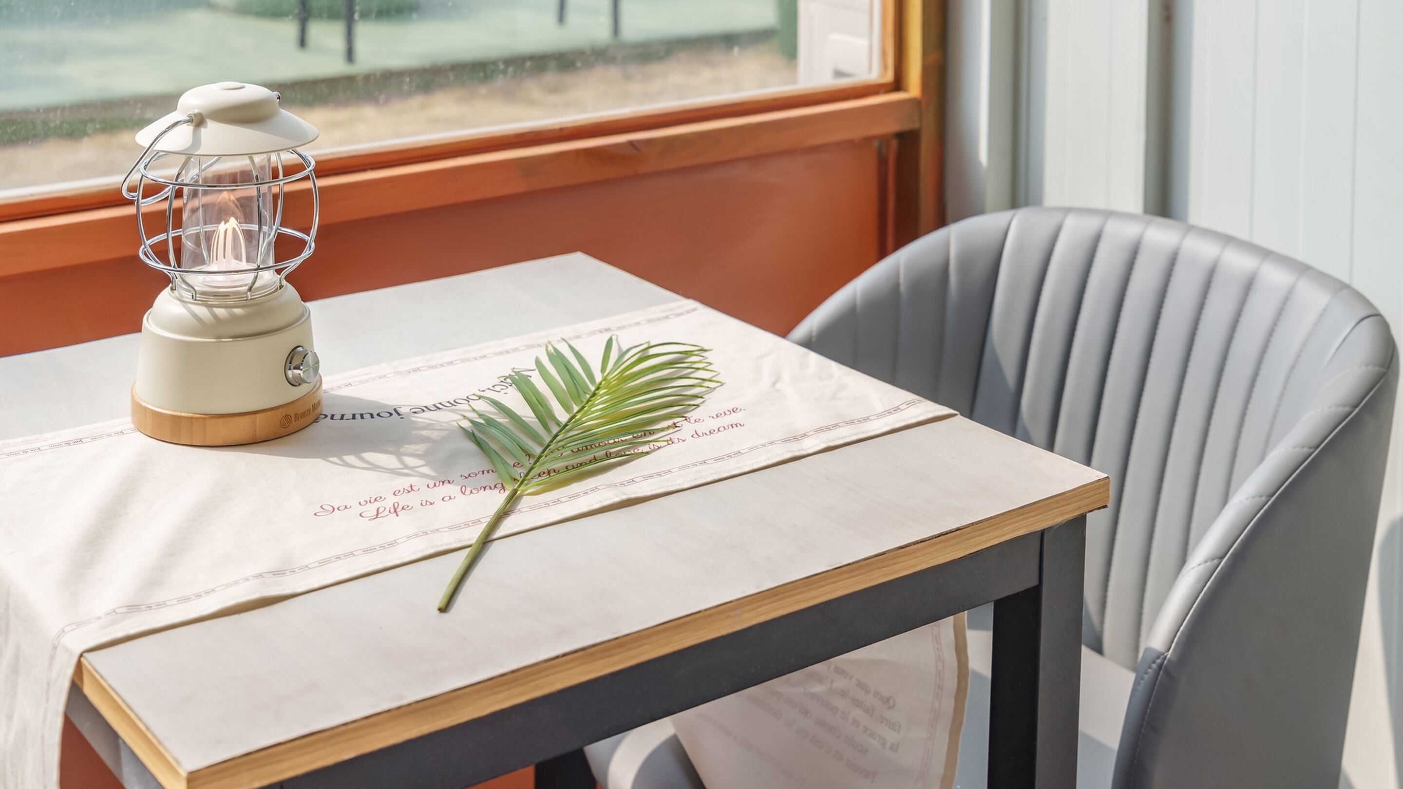 A table with a white tablecloth, a small lamp, a book, and a palm leaf.