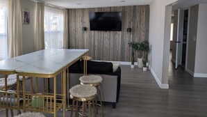Una sala de estar moderna con pared de paneles de madera, televisor de pantalla plana, mesa de comedor con taburetes altos y un sofá.