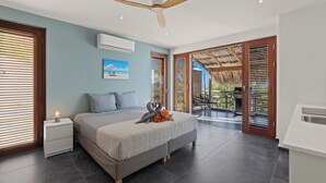 Une chambre moderne avec un lit, des tables de chevet, un ventilateur de plafond et une vue sur l’extérieur.