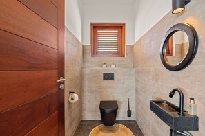 Een badkamer met een houten deur, een raam, een toilet, een wastafel en een spiegel.