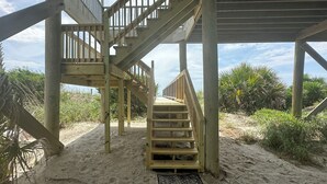A wooden staircase leading to a beach area with a sandy path and palm trees.