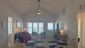 A dining area with a glass-top table, white chairs, and a ceiling fan.