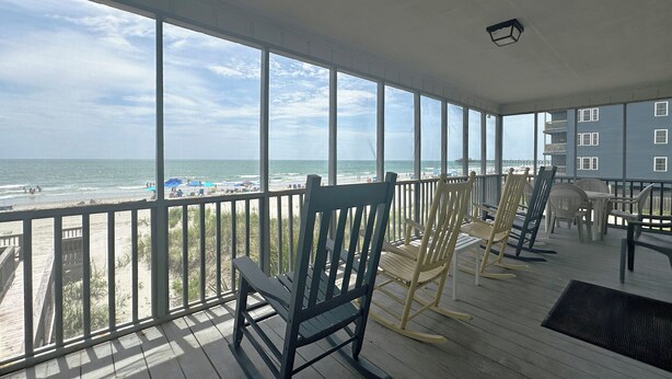 A wooden deck with rocking chairs overlooking a beach.