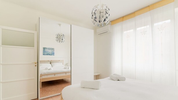 Un dormitorio con cama, armario, espejo, candelabro y un cuadro.