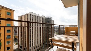 Un balcón con una mesa y sillas de madera, barandilla de metal y vistas a edificios cercanos.