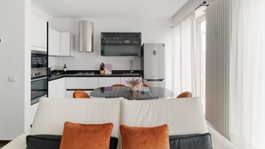 A modern kitchen with white cabinets, a black countertop, and a dining area with a glass table and orange cushions. - GuestHost - Superior Apt with balcony and parking (Milano)