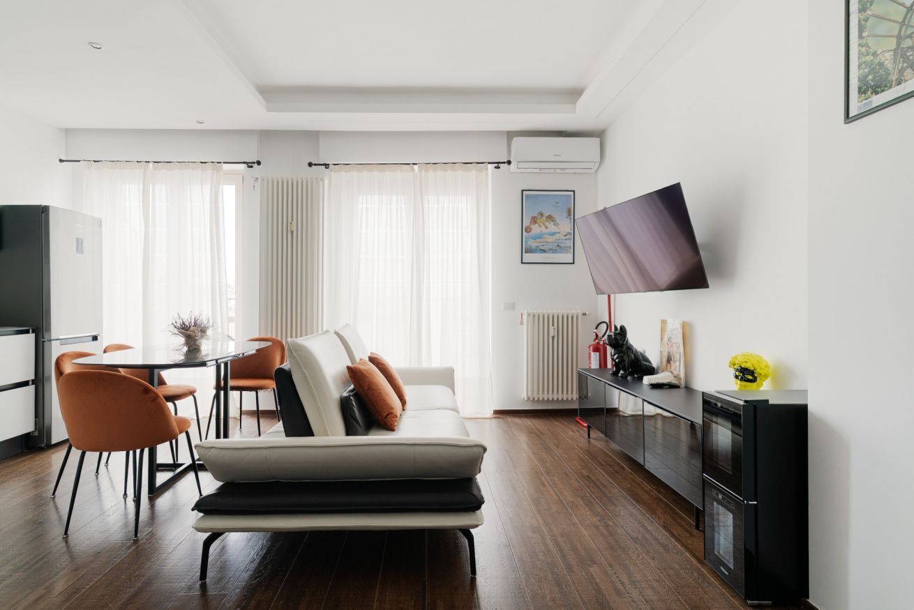 A modern living room with a sofa, dining table, chairs, a TV, and a kitchen area.