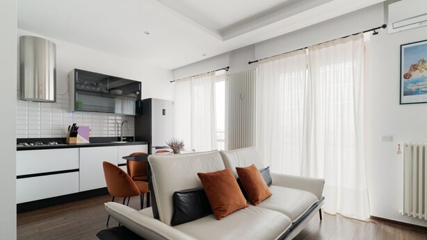 A modern living room with a sofa, a dining table, and a kitchen area. - GuestHost - Superior Apt with balcony and parking (Milano)