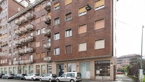 A multi-story residential building with balconies, a gated entrance, and parked cars. - GuestHost - Superior Apt with balcony and parking (Milano)