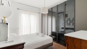 A modern hotel room with a bed, bedside table, wardrobe, and a view through a glass door. - GuestHost - Superior Apt with balcony and parking (Milano)