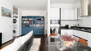 A modern kitchen with white cabinets, a stainless steel range hood, and a dining area with a glass table and chairs. - GuestHost - Superior Apt with balcony and parking (Milano)
