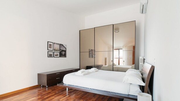 Quarto moderno com uma cama grande, um guarda-roupa, uma mesa de cabeceira e um espelho fixado na parede.