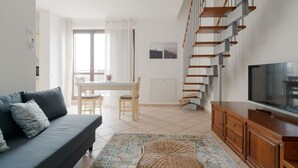 Uma sala de estar moderna com sofá, televisão, escada de madeira e área de refeições.
