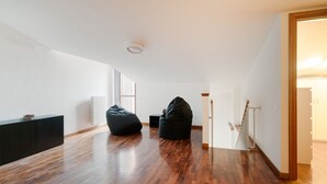Um amplo loft com pé direito alto, uma escada e duas poltronas de chão.