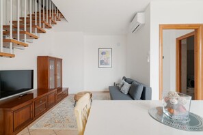 Un salon comprenant un escalier, un téléviseur, un meuble, un canapé et une table à manger.