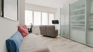 A modern living room with a sofa, a recliner, a flat-screen TV, and a sliding glass door. - GuestHost - Cozy 78 sqm apartment, able to accommodate up to 4 people, located on the first floor of a building with lift.The property is located 650m from the Famagosta stop of the green metro line M2, which allows you to reach Piazza Duomo, Central Sta (Milano)