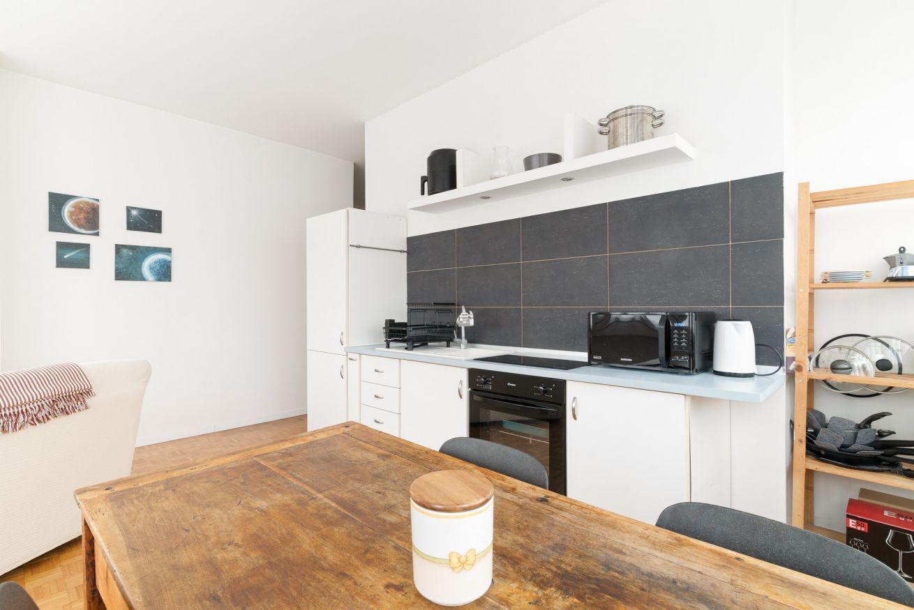 Une cuisine moderne avec une table en bois, des placards blancs, un four à micro-ondes et une machine à café.