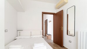 A bedroom with a bed, a wooden door, a mirror, and a radiator. - GuestHost - Cozy 78 sqm apartment, able to accommodate up to 4 people, located on the first floor of a building with lift.The property is located 650m from the Famagosta stop of the green metro line M2, which allows you to reach Piazza Duomo, Central Sta (Milano)