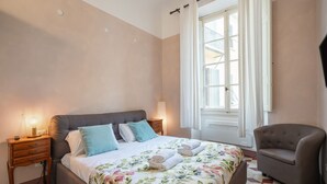Ein Schlafzimmer mit Bett, Nachttischen, einem Sessel und einem Fenster mit Vorhängen.