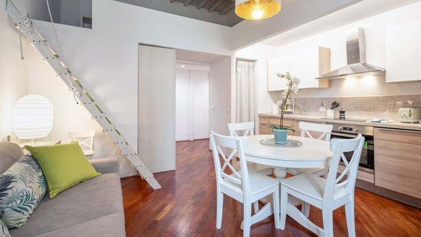 Eine moderne Küche mit weißen Schränken, einem Esstisch mit weißen Stühlen und einer Treppe, die in eine obere Etage führt.