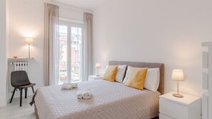 A hotel room with a bed, two bedside tables, a chair, a radiator, and a window with curtains.