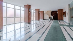 A spacious lobby with a marble floor, wooden pillars, and a staircase leading to an upper level.