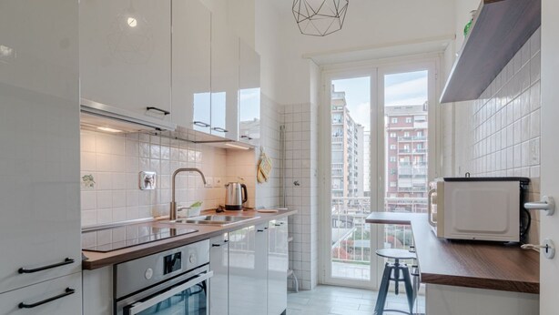 A modern kitchen with white cabinets, a wooden countertop, and a view of the city through a large window.