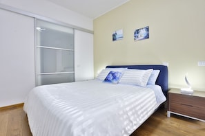 A bedroom with a bed, a nightstand, a drawer, a sliding door, and two wall-mounted pictures.