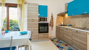 A kitchen with blue cabinets, a microwave, an oven, a sink, and a dining area with a table and chairs.