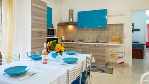 A modern kitchen with blue cabinets, a central island, and a dining area with blue tableware.