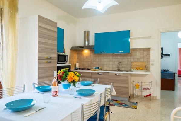 Une cuisine moderne avec des meubles bleus, un îlot central et un coin repas agrémenté de vaisselle bleue.