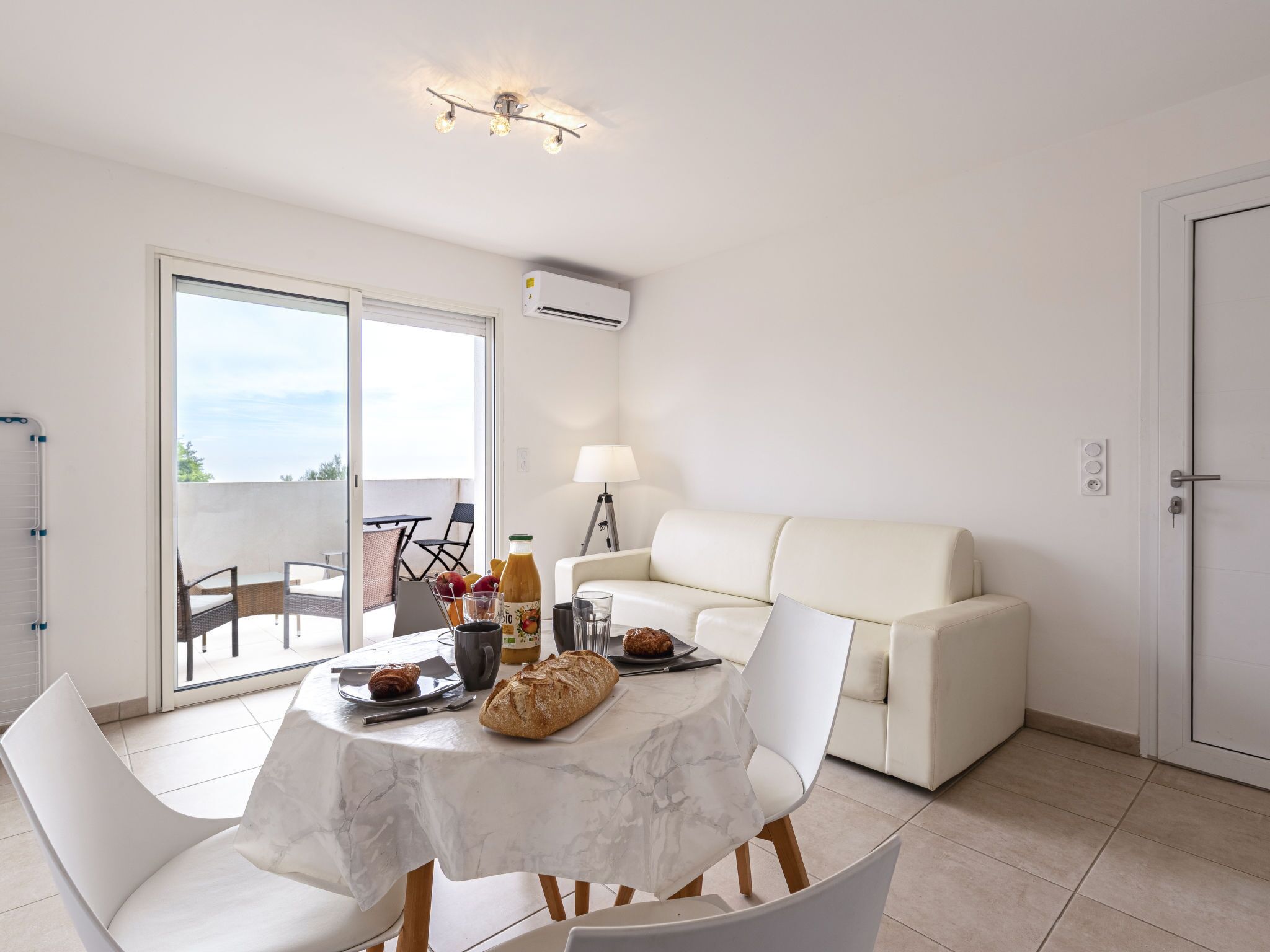 En moderne stue med en hvid sofa, et spisebord med et marmortæklæde, og en balkon med udsigt.