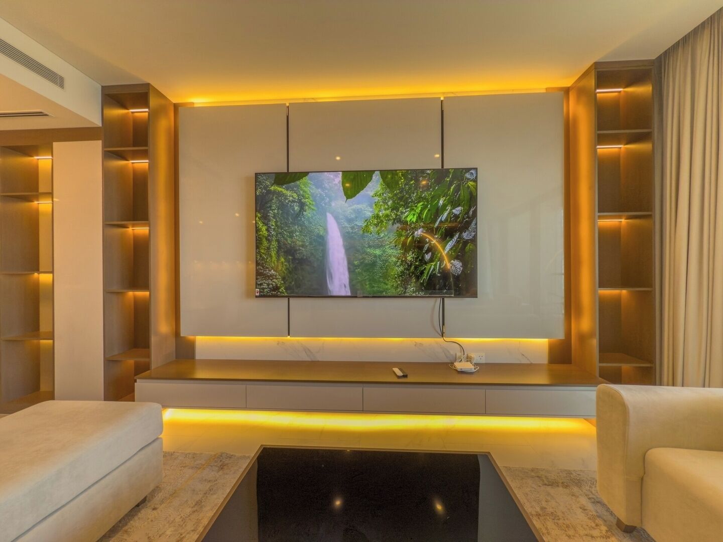 Una sala de estar moderna con un televisor de pantalla plana montado en la pared, un sofá y una mesa de centro.
