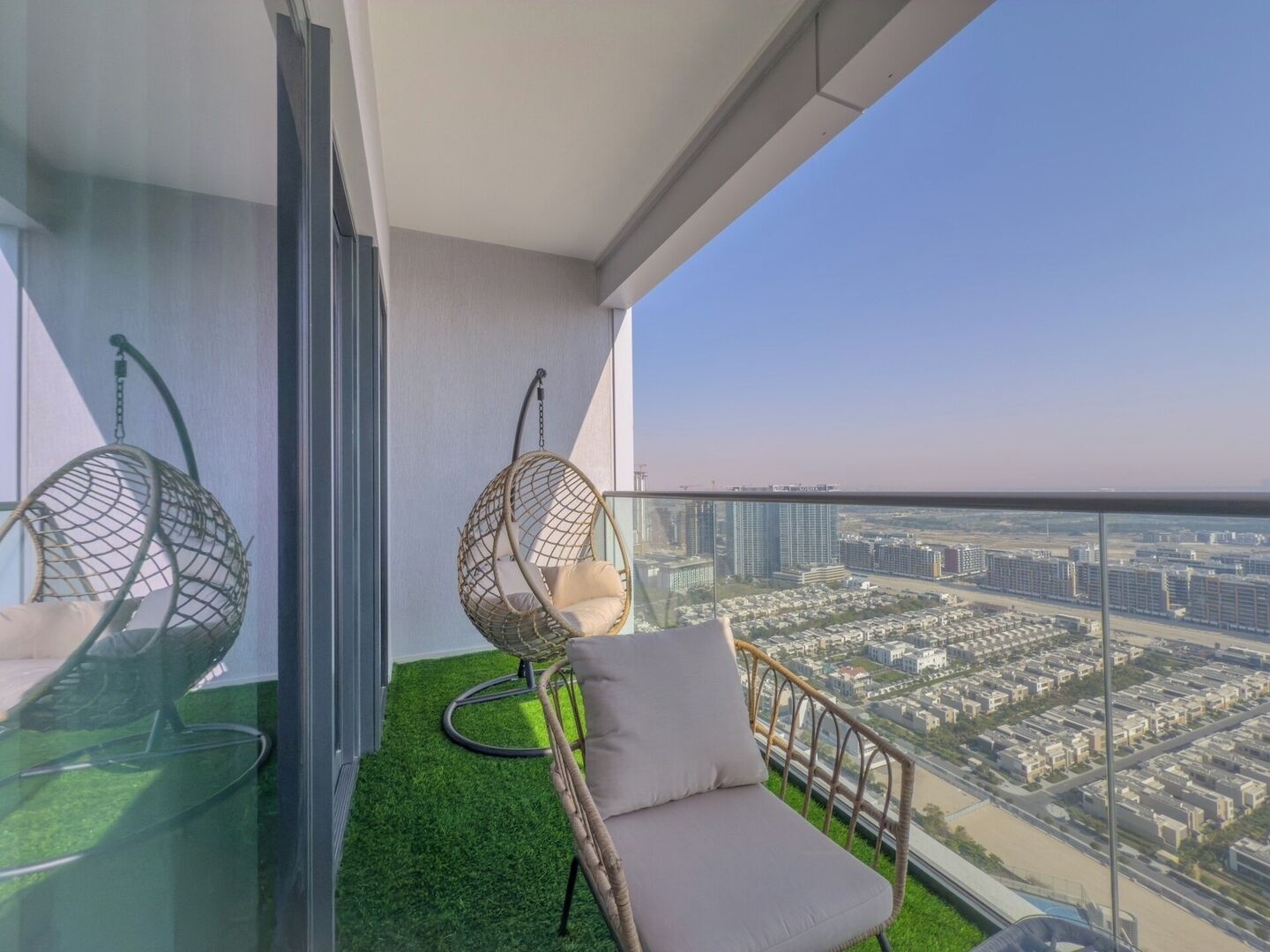 Ein Balkon mit einer Hängematte, einem gepolsterten Stuhl, einer Glastür und Blick auf eine Stadtlandschaft.